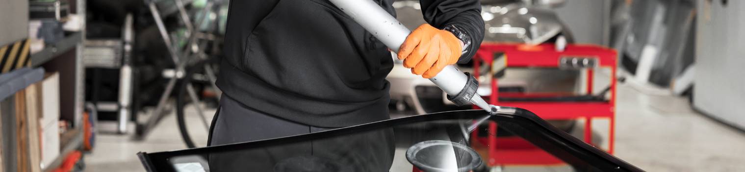 Glazier applying rubber sealing to windshield in garage, clo