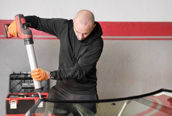 Glazier applying rubber sealing to windshield in garage, clo